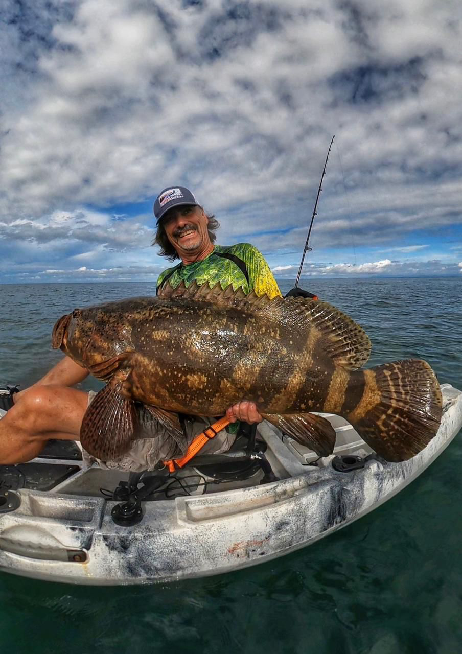 Older kayak angler laughing behind a giant saltwater grouper
